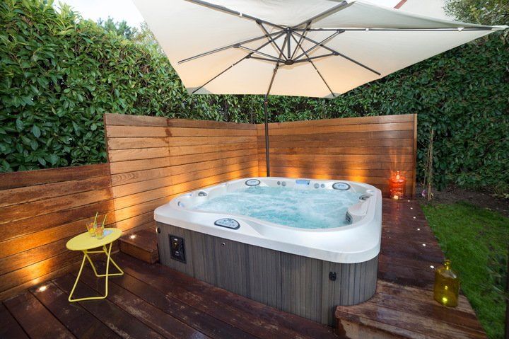 ideas for hot tub privacy with hot tub in a backyard surrounded by plants and wooden walls with an umbrella overtop